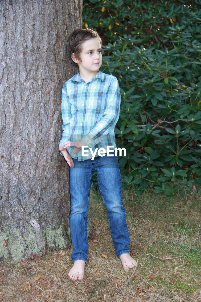 FULL LENGTH PORTRAIT OF BOY STANDING BY TREE TRUNK