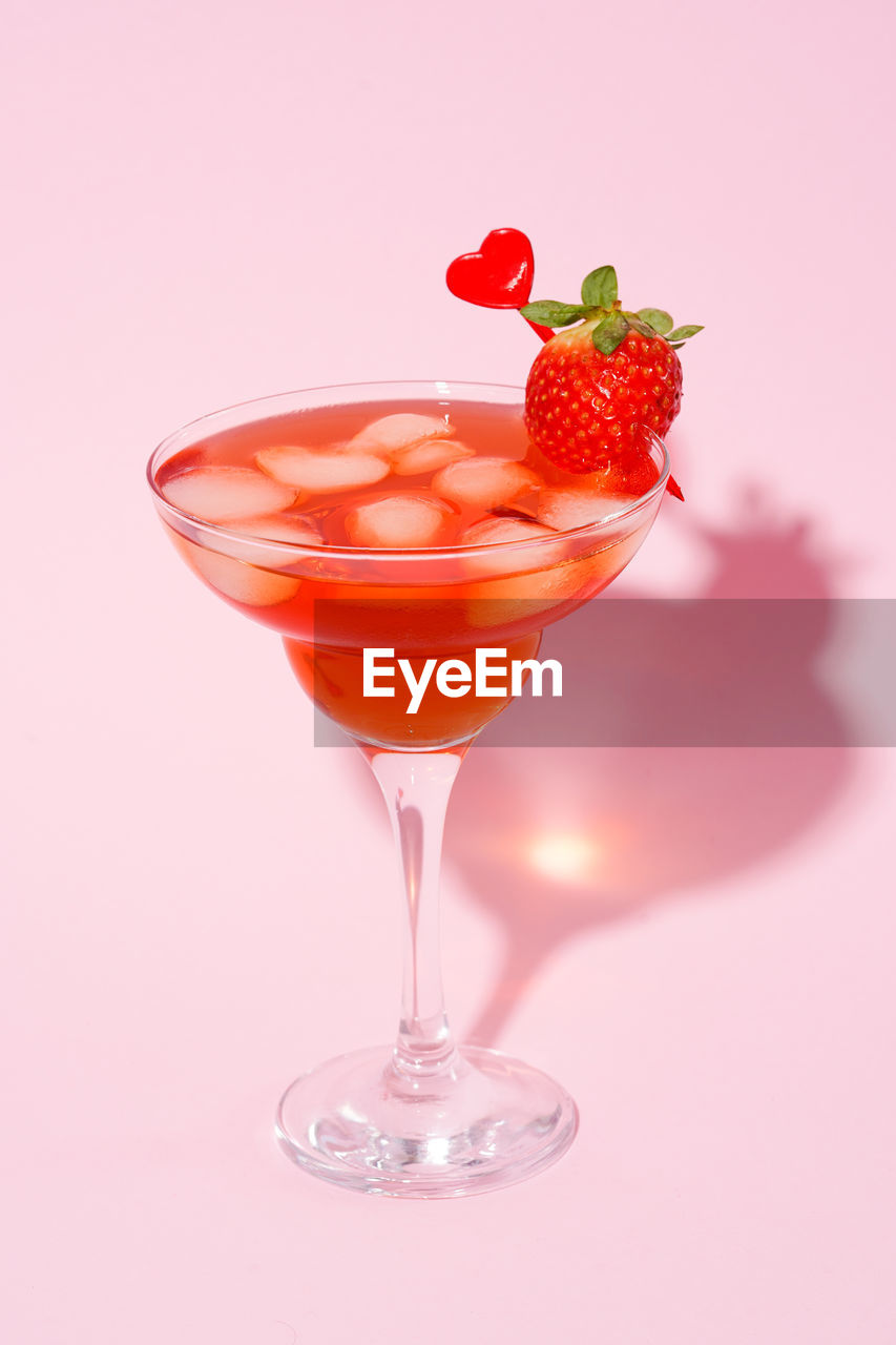 Valentine day cocktail with red heart in martini glass on pink background