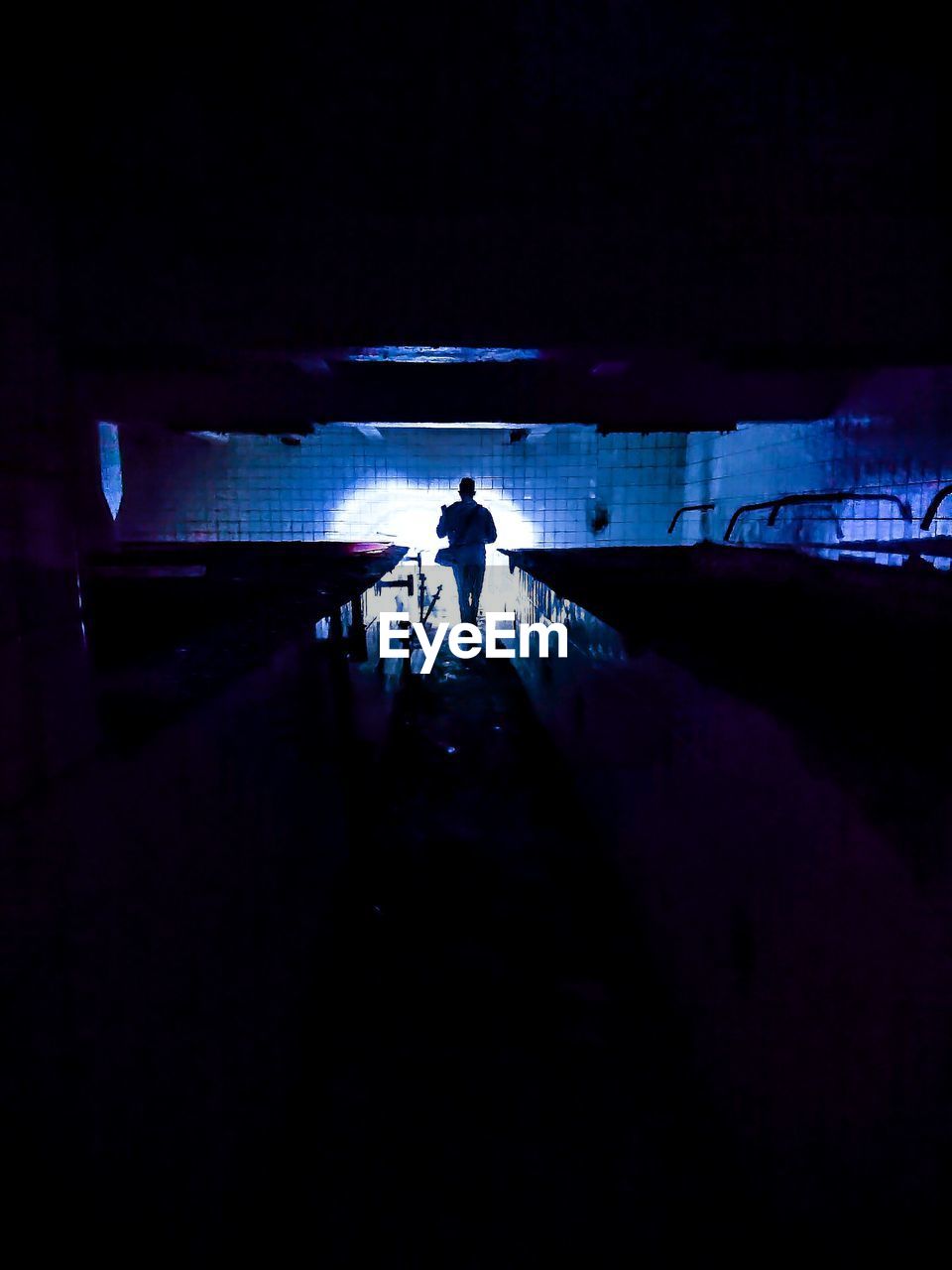 SILHOUETTE OF MAN STANDING IN ILLUMINATED TUNNEL