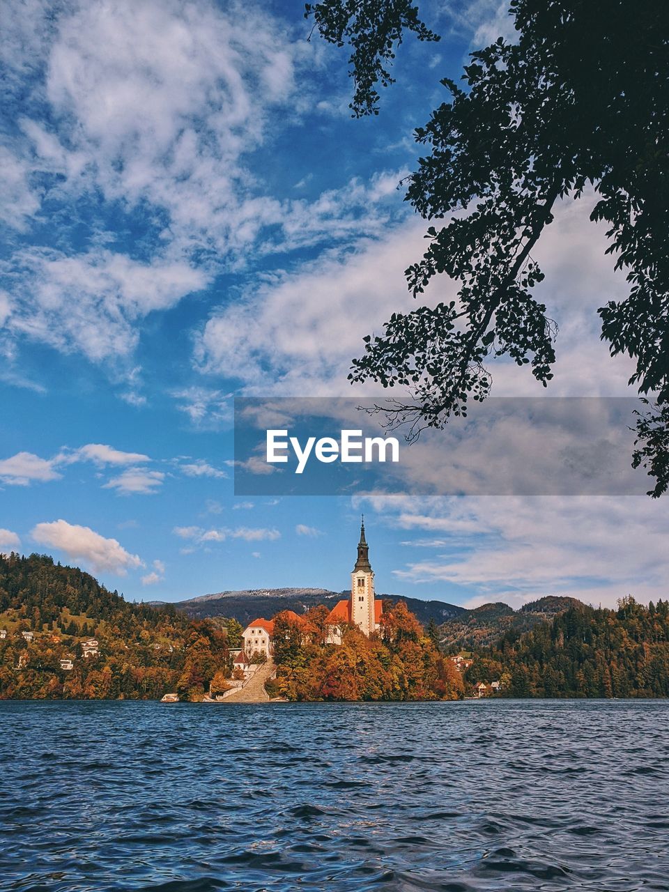 Buildings at waterfront on lake bled against cloudy sky in autumn.