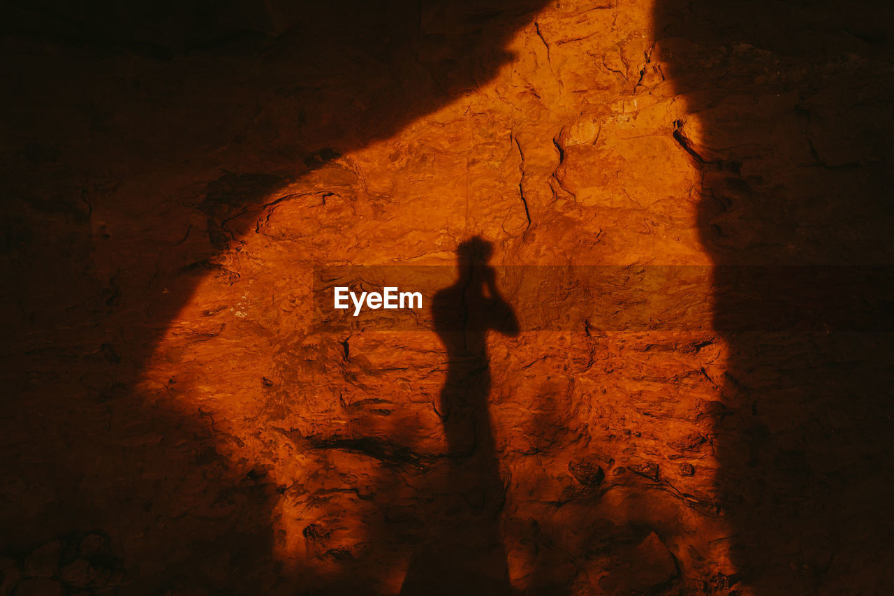 Silhouette of person against red cave entrance at sunset in desert