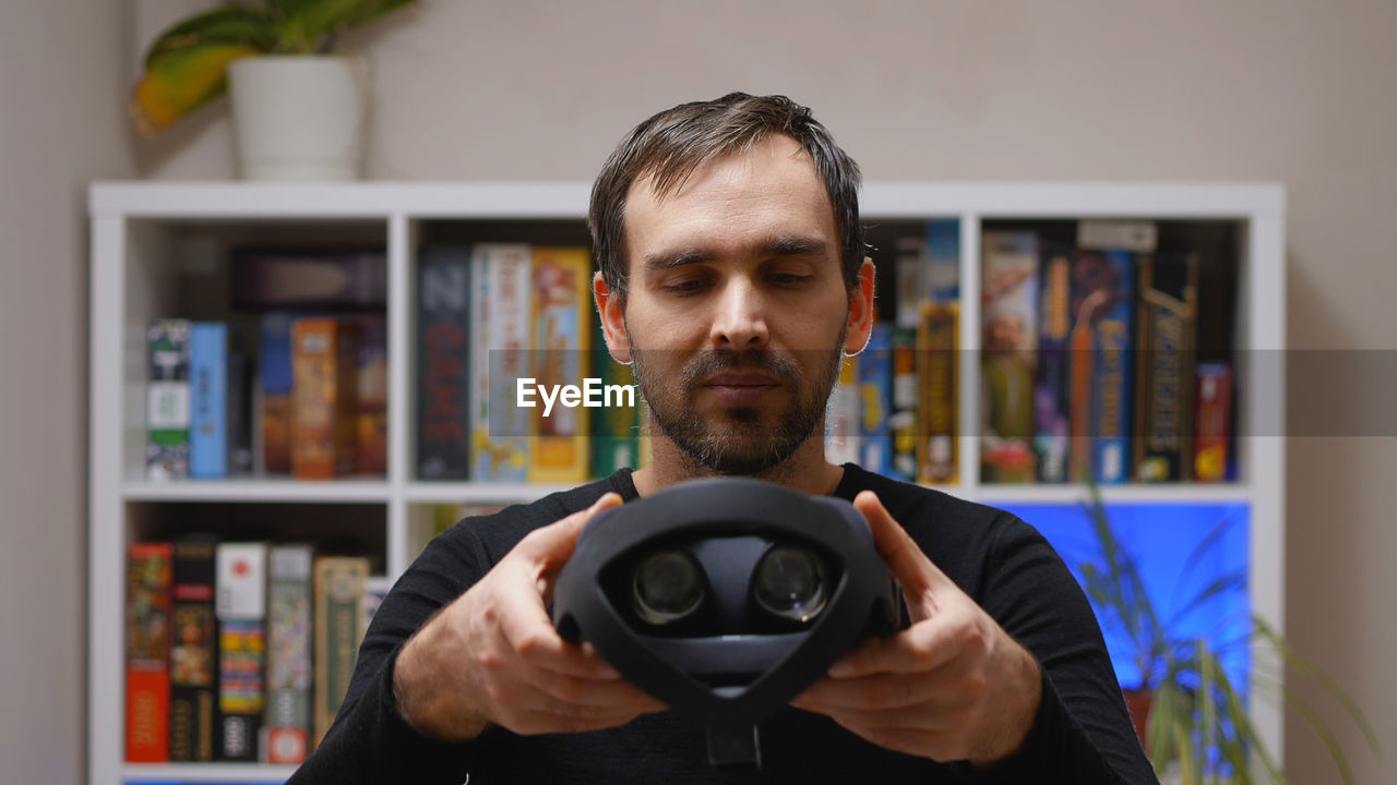 A caucasian man in a black hoodie holding a virtual reality helmet