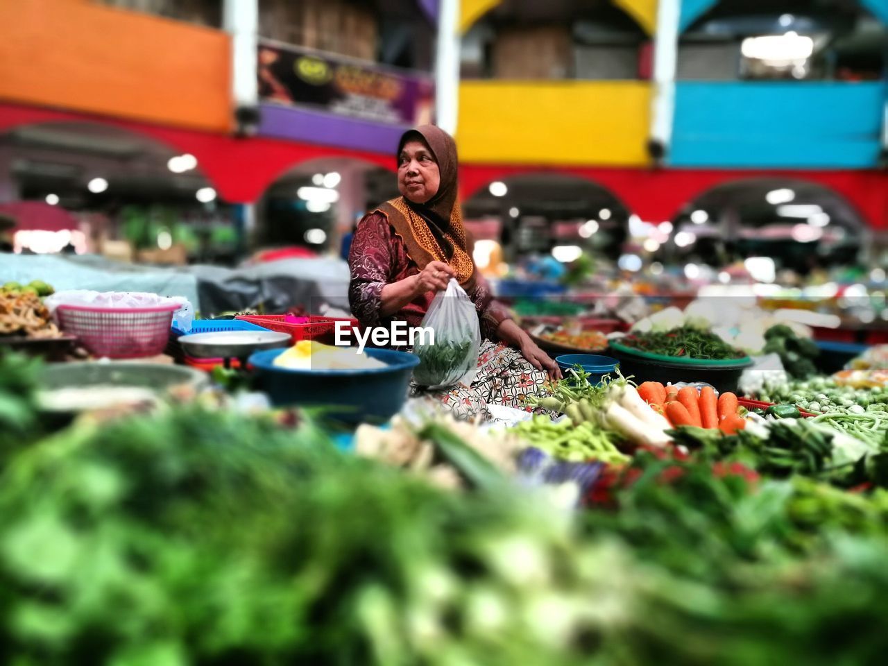 Mature owner surrounded with vegetables at supermarket