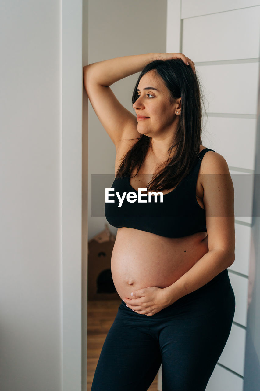 Happy pregnant woman stands at home.