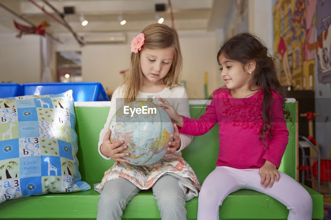 Girls looking at globe while sitting on green seat at child care