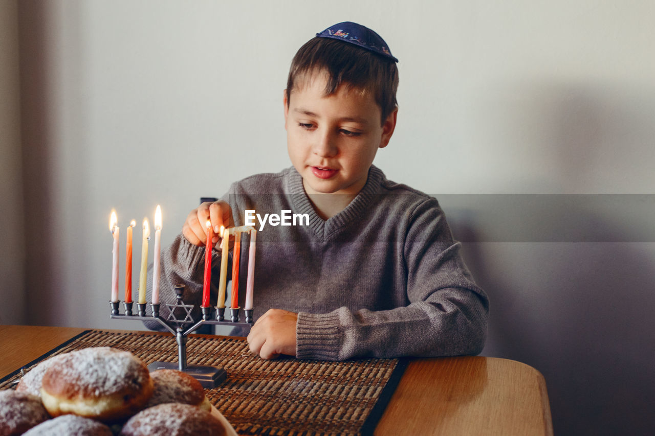 Boy in kippah lighting candles on a menorah for traditional winter jewish hanukkah holiday