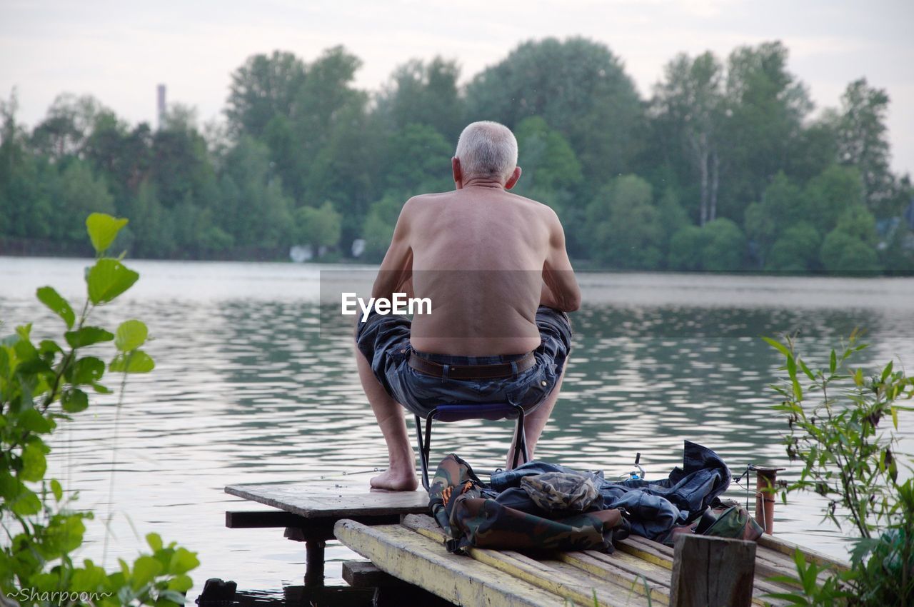 Rear view of senior man sitting on pier by lake