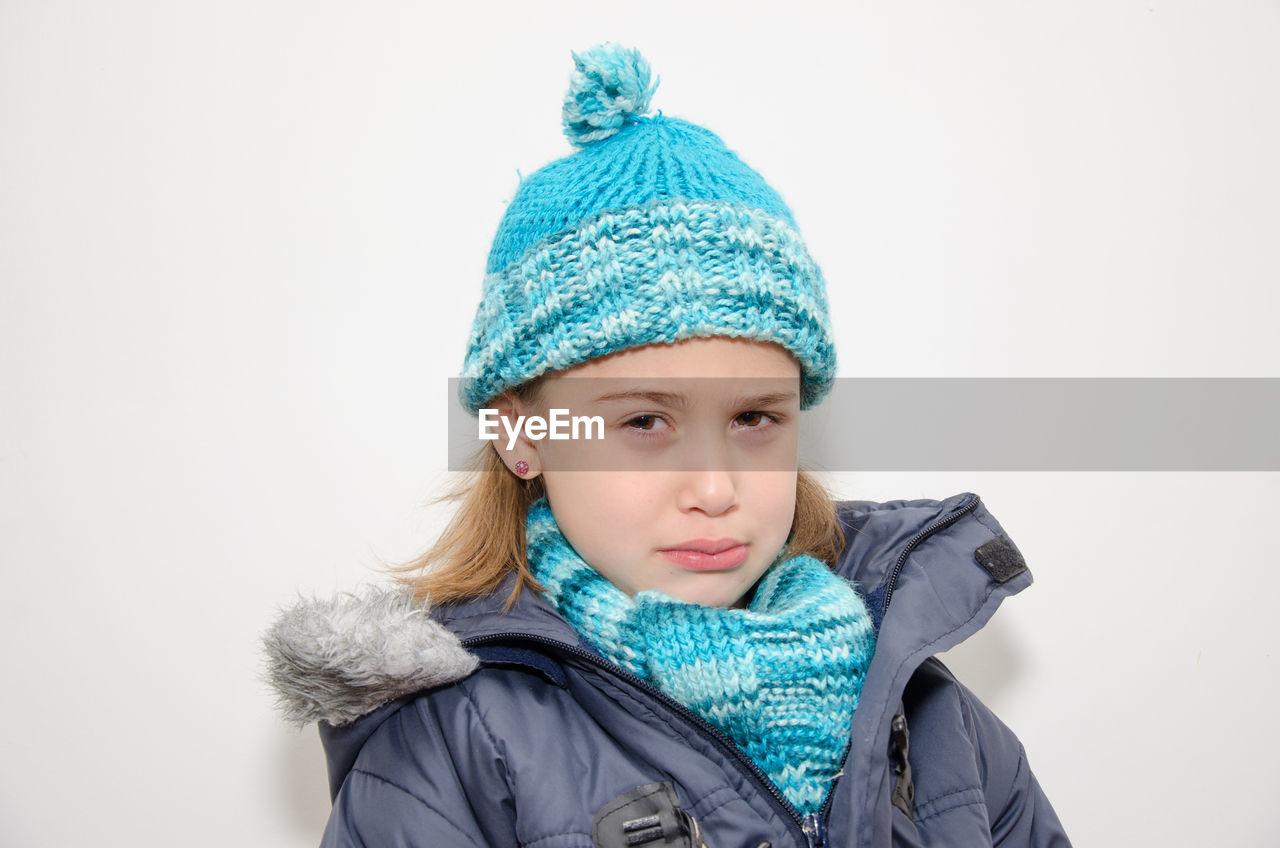 Portrait of sad girl in warm clothes against white background