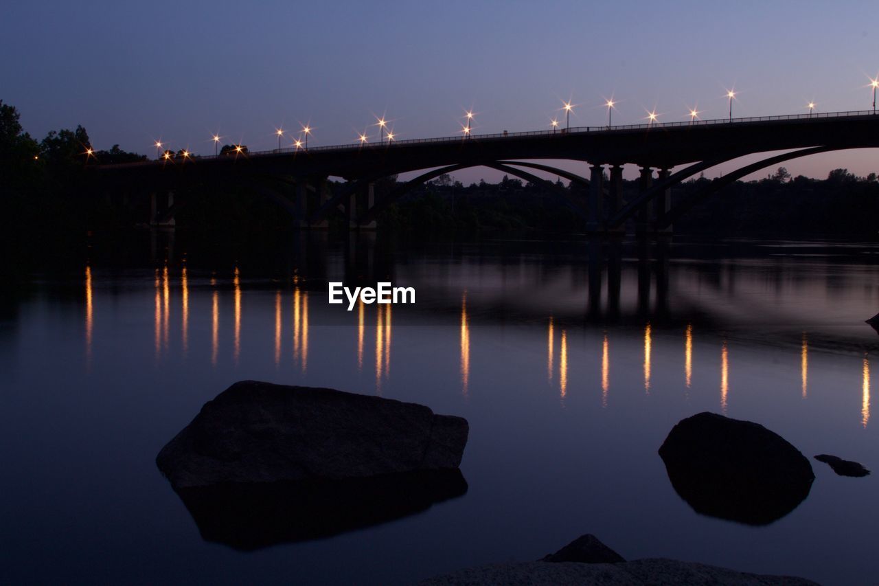 Illuminated bridge over river against sky at night