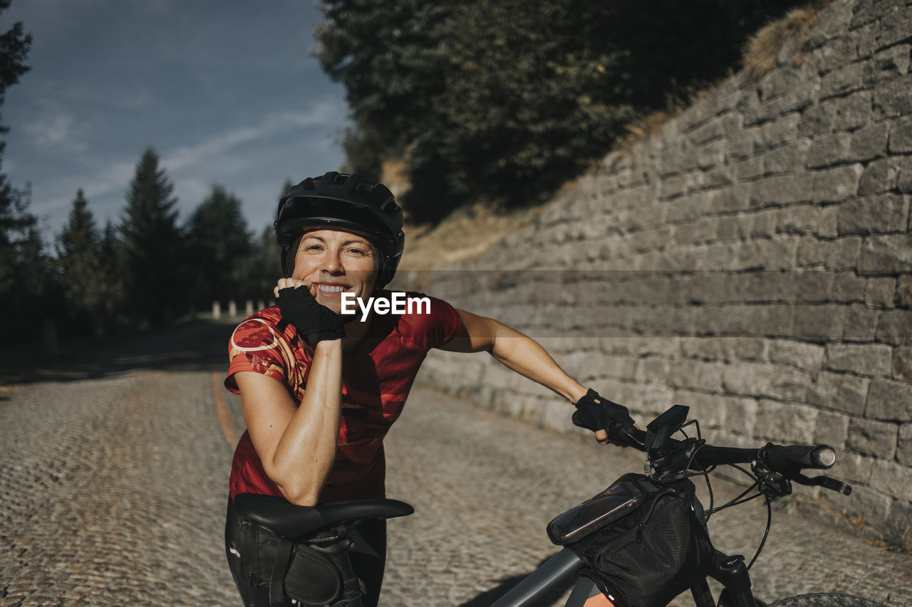 Smiling woman wearing helmet leaning on bicycle seat