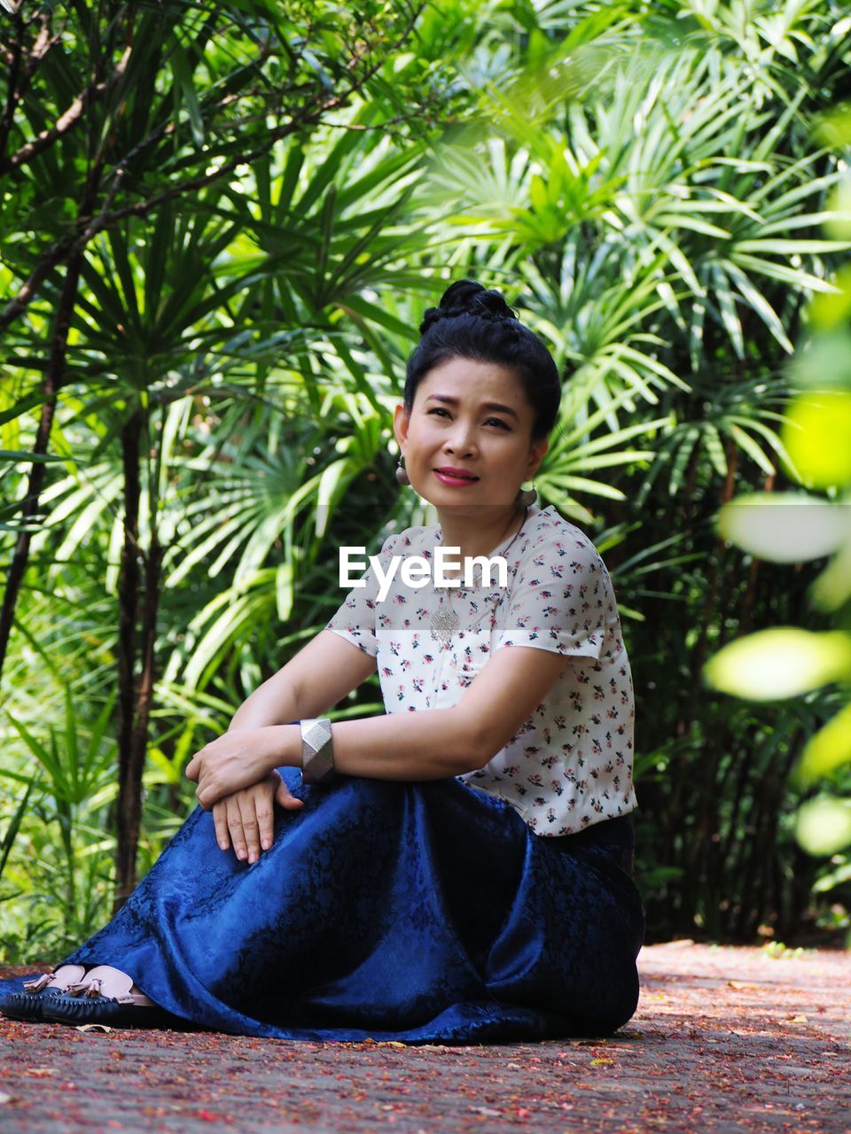 PORTRAIT OF A SMILING YOUNG WOMAN SITTING AGAINST PLANTS