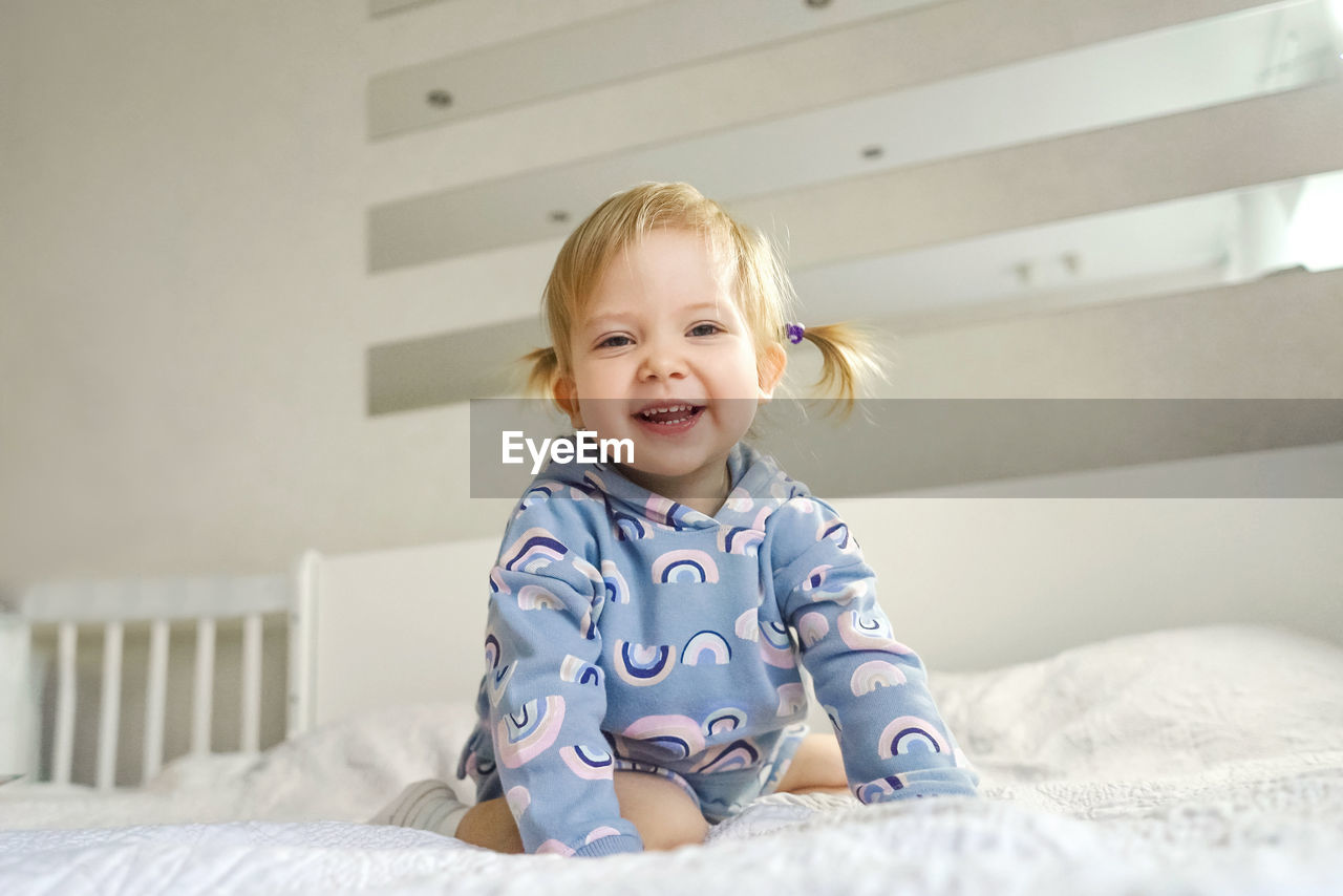 Low angle portrait of smiling girl sitting on bed