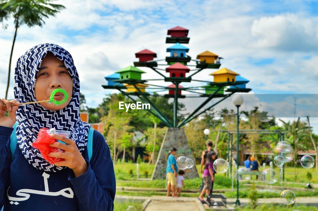 Portrait of young woman blowing bubbles in park