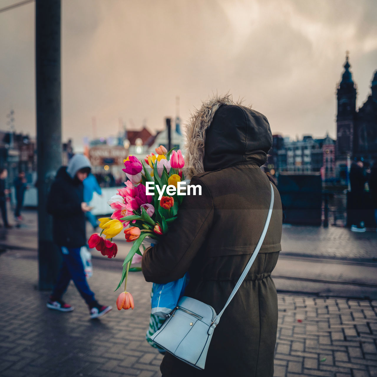 REAR VIEW OF WOMEN STANDING ON STREET IN FRONT OF RED FLOWERING