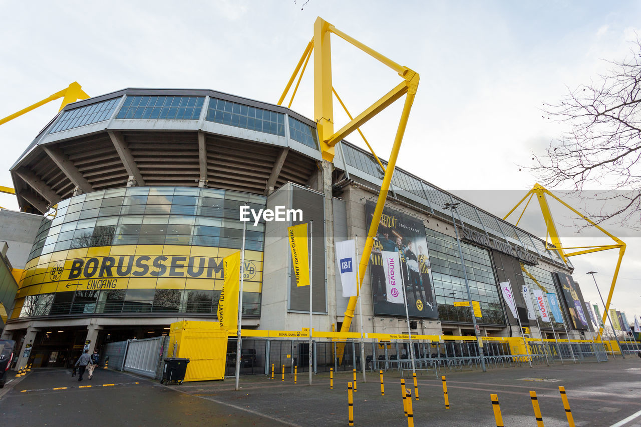 architecture, sport venue, transport, built structure, sky, industry, stadium, building exterior, transportation, city, yellow, arena, nature, vehicle, business, building, outdoors, business finance and industry, facade, day, mode of transportation