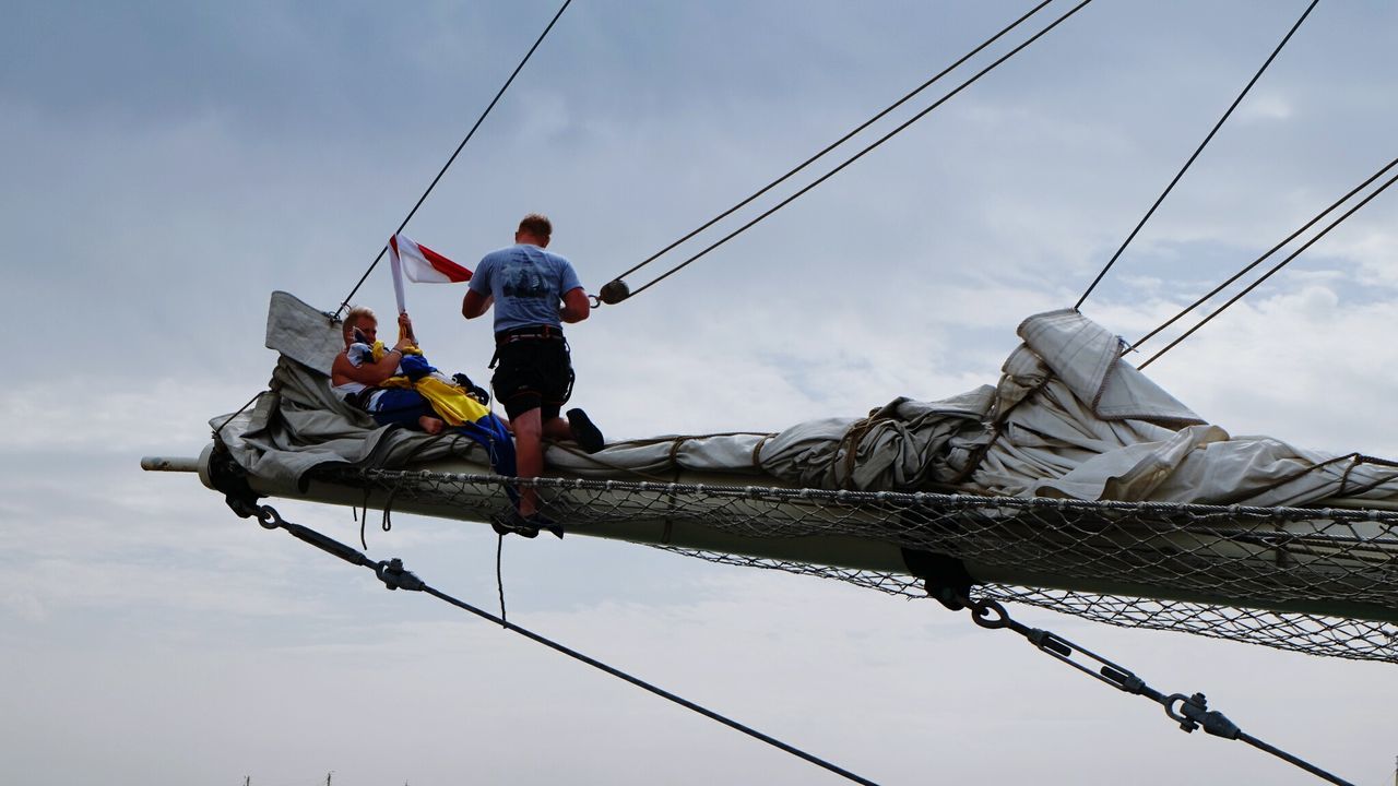 Low angle view of people on ship against cloudy sky