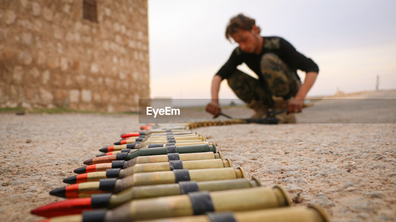 Full length of man arranging bullets on land against sky