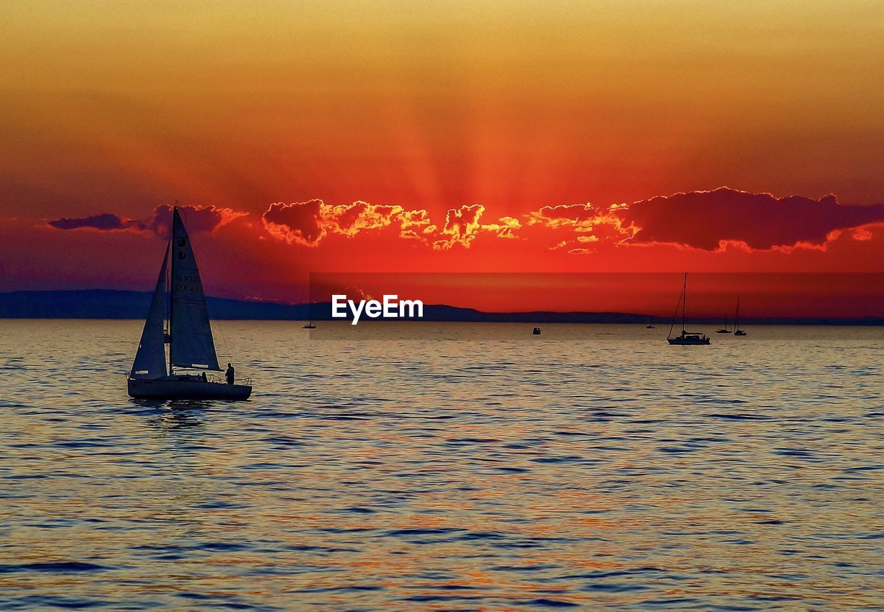 Sailboat sailing in sea against sky during sunset