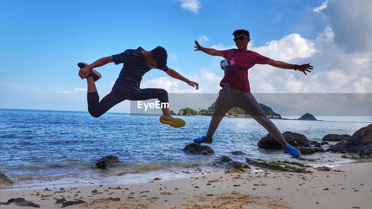 LOW ANGLE VIEW OF MEN JUMPING ON BEACH