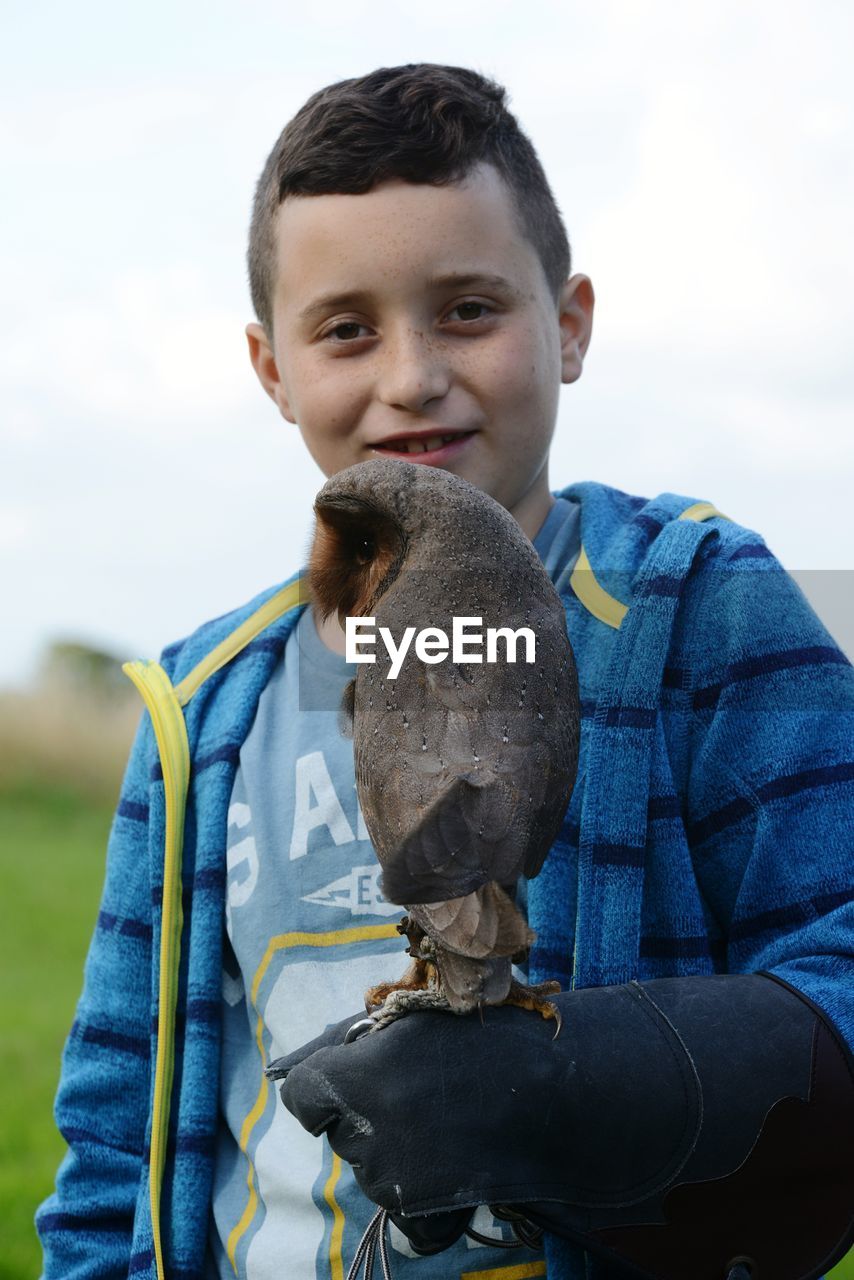 Portrait of boy holding owl against sky