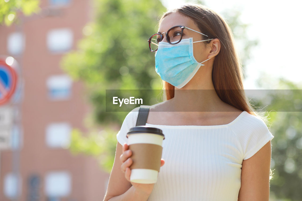 Woman wearing mask standing with disposable cup