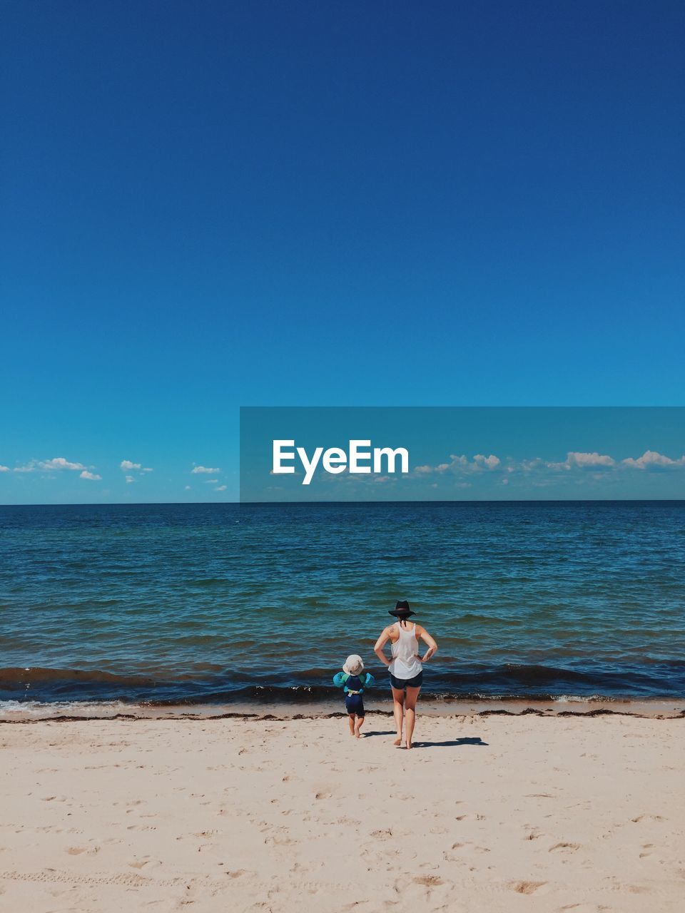 REAR VIEW OF MAN STANDING ON BEACH