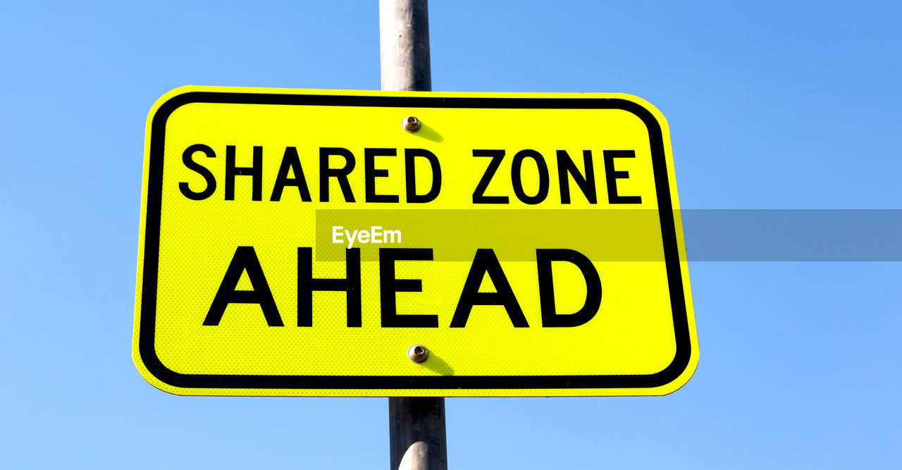 Low angle view of road sign against clear blue sky