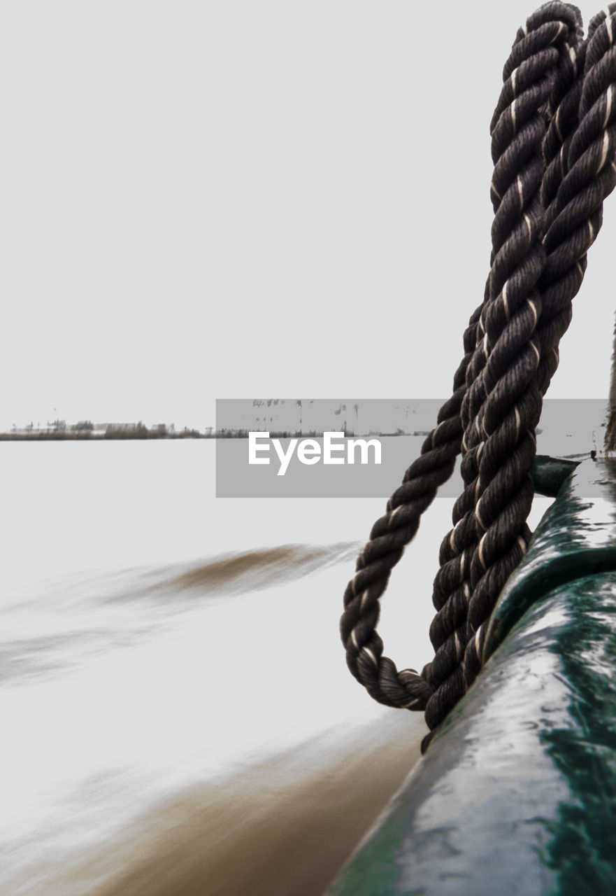 Rope hanging on boat sailing in sea against clear sky