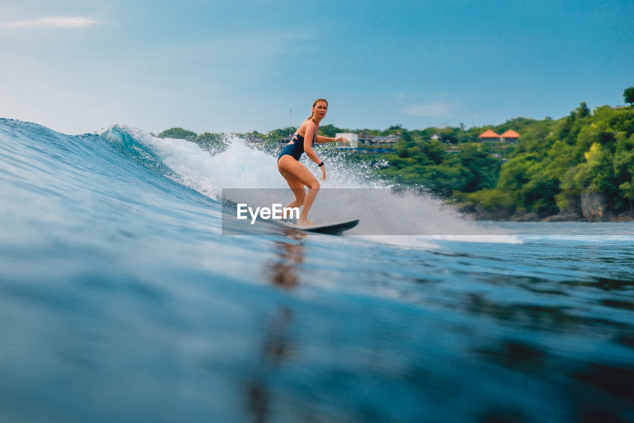 side view of woman surfing in sea against sky