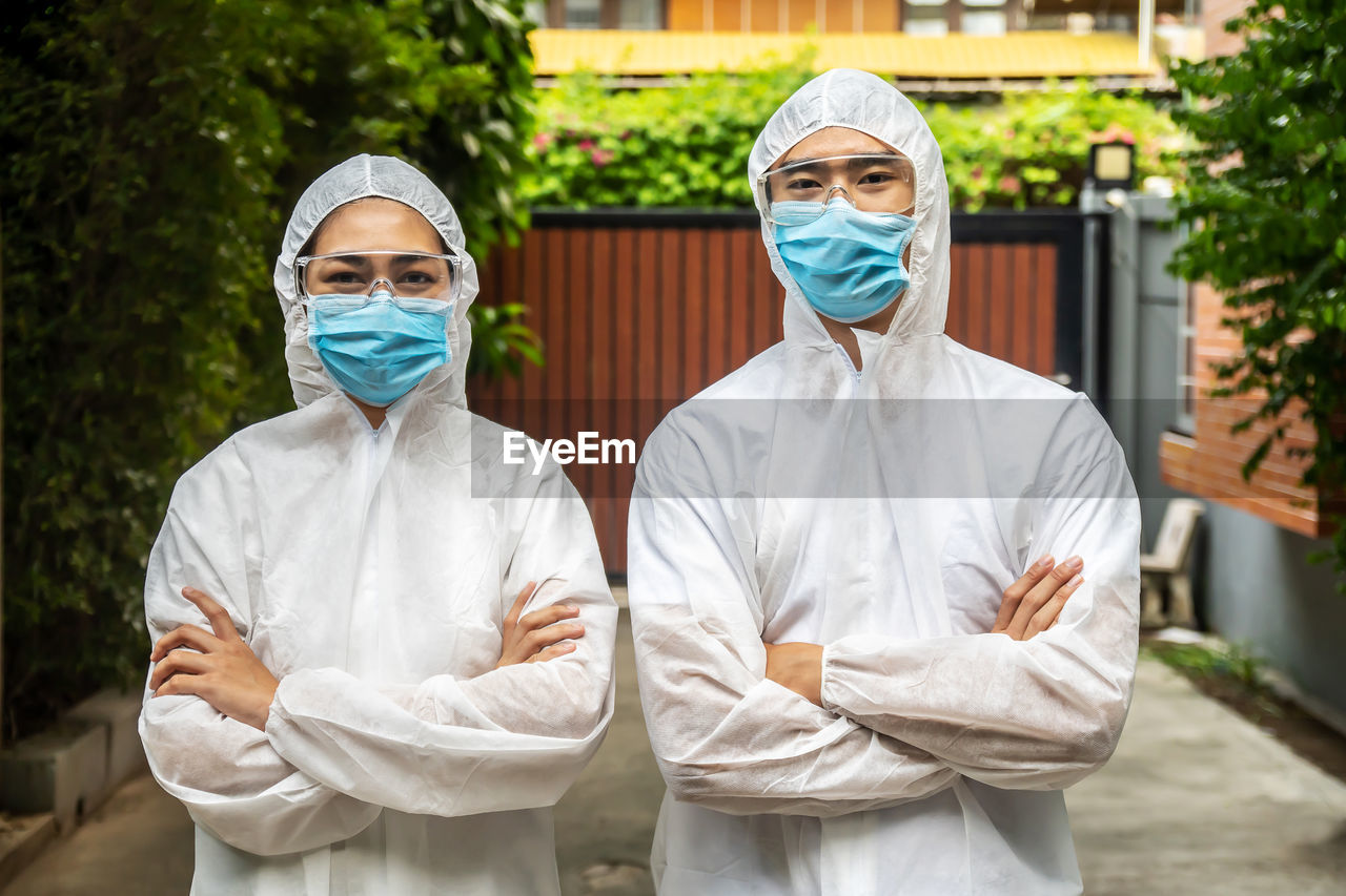 Portrait of man and woman wearing protective suit with mask standing outdoors