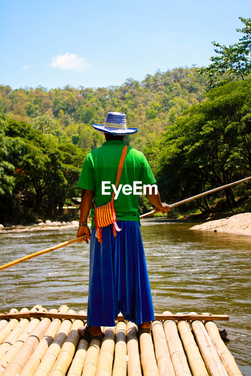 Rear view of man standing on traditional boat in lake