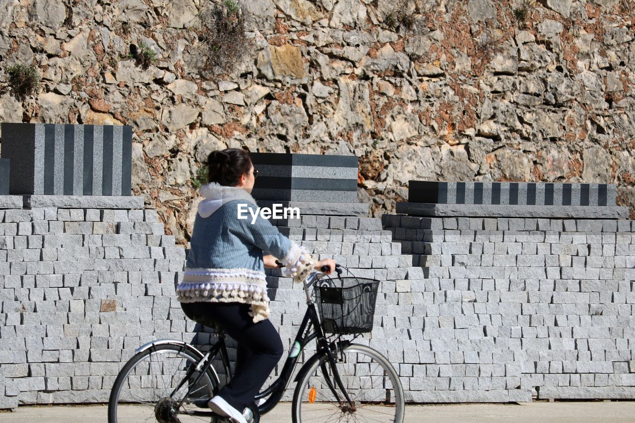 REAR VIEW OF WOMAN ON BICYCLE AGAINST WALL