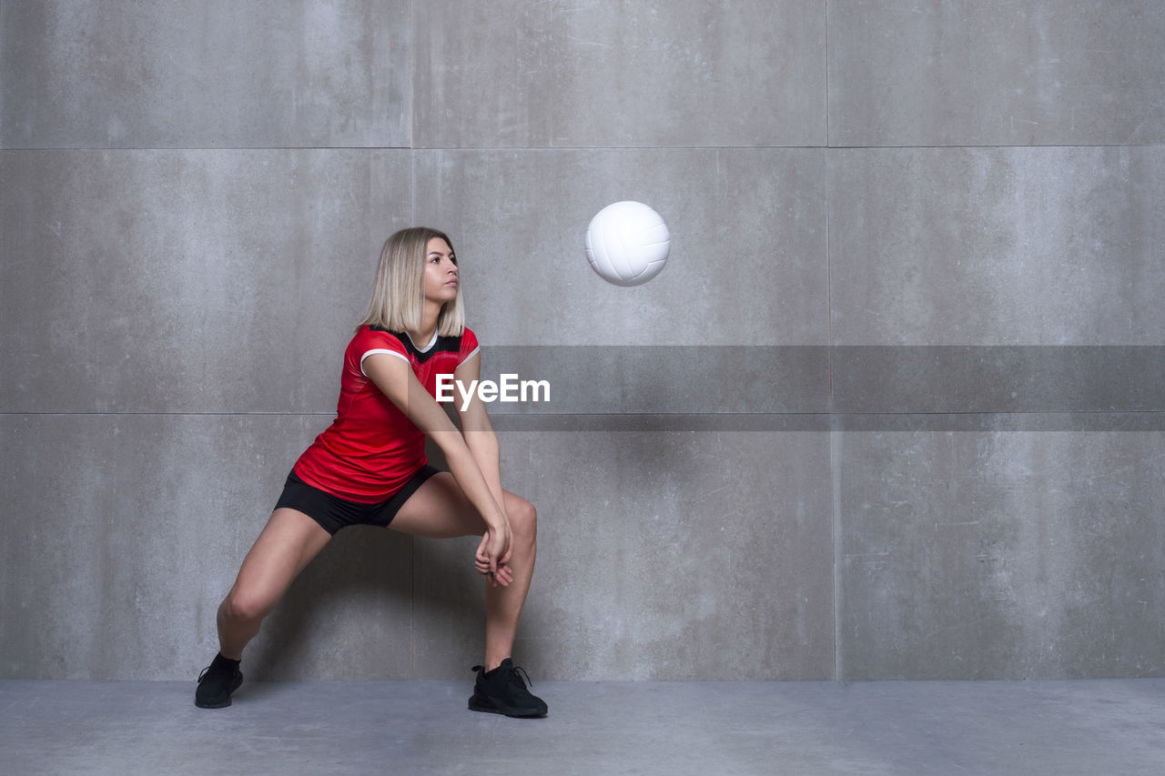 Full length of young woman playing volleyball by wall