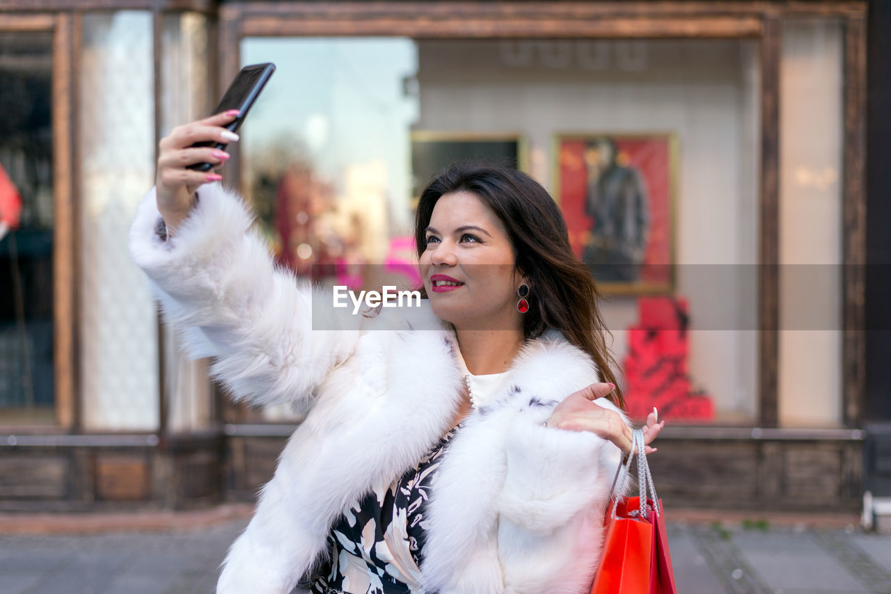 Smiling woman taking selfie while holding shopping bag while holding shopping bag outdoors