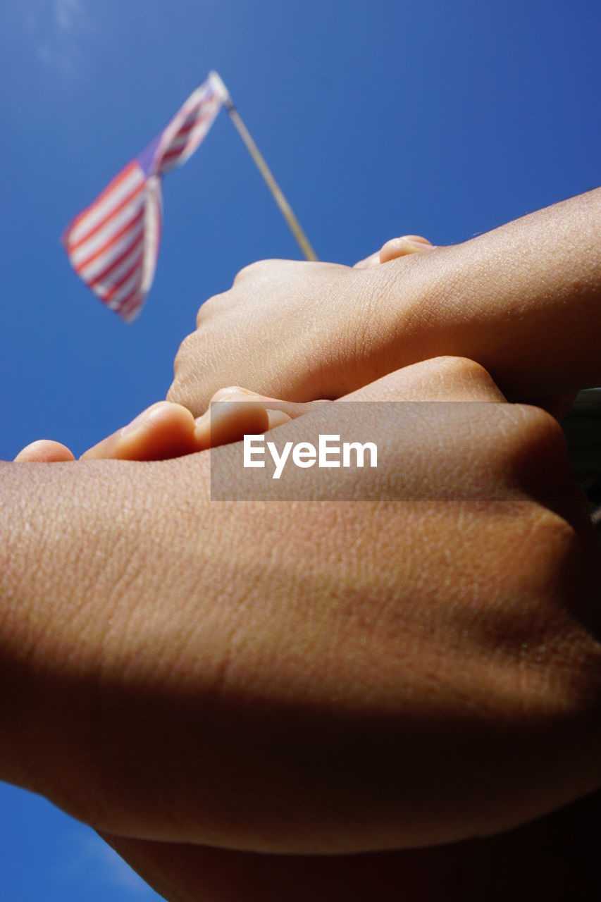 CLOSE-UP OF HAND HOLDING FLAG AGAINST BLUE SKY
