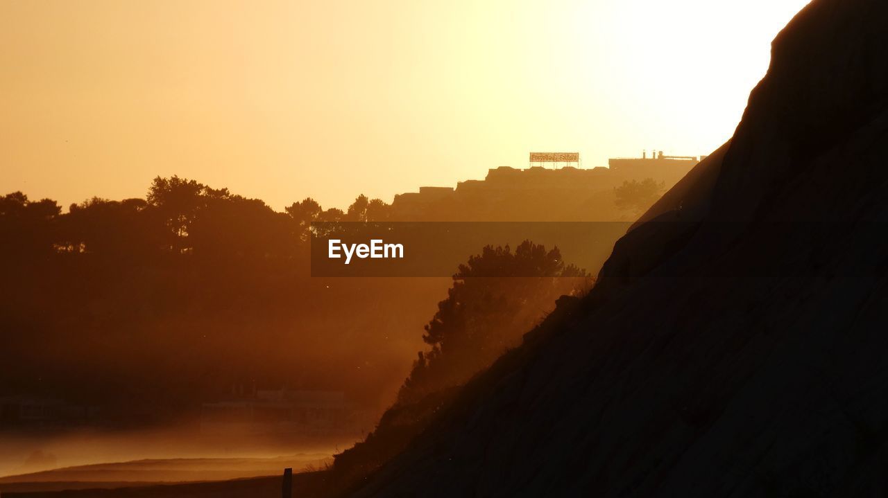 Silhouette trees and buildings against sky during sunset