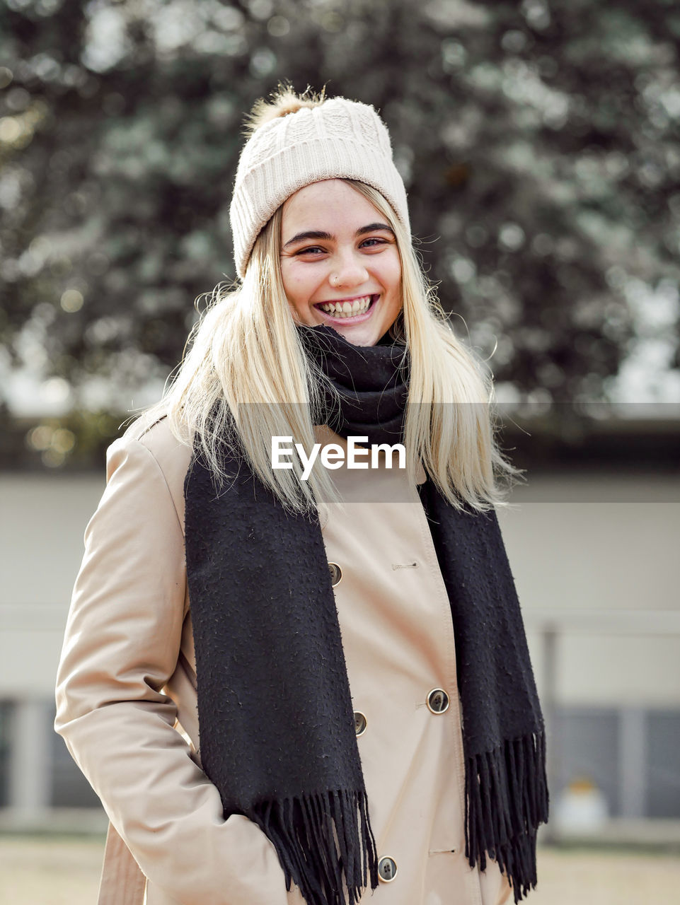 Young sincere blond female in knitted hat and warm clothes looking at camera in back lit