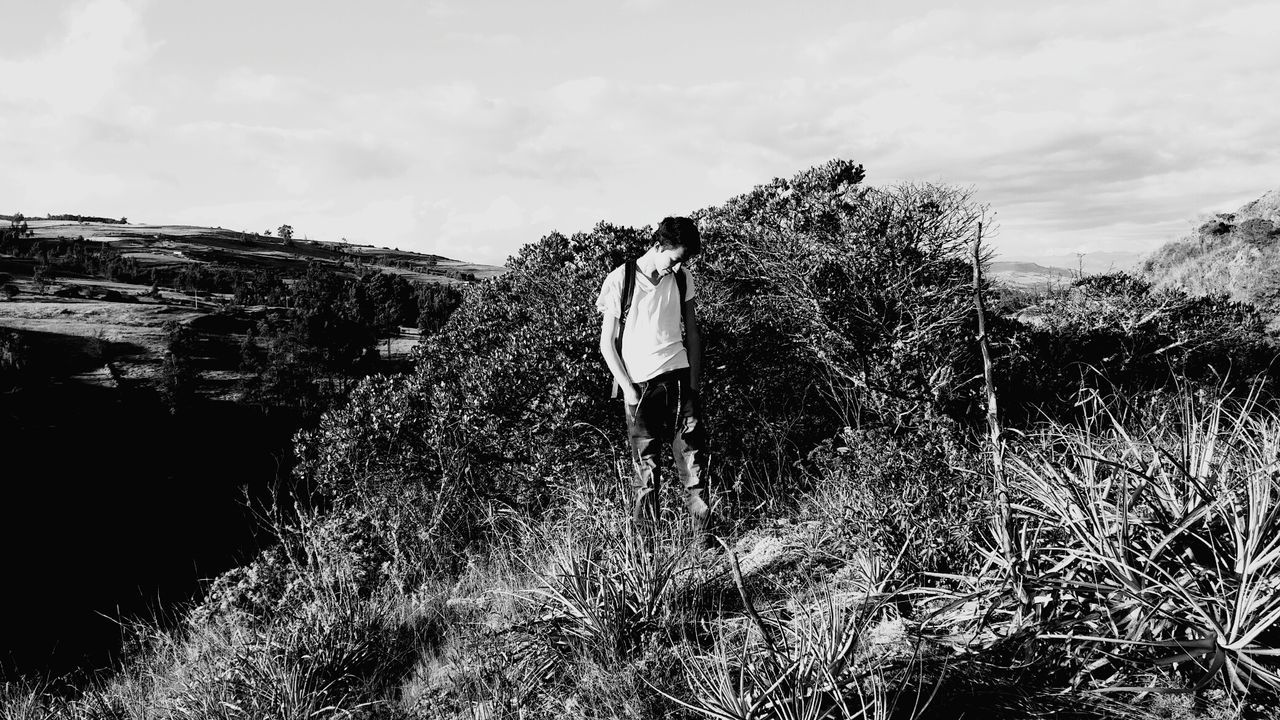 Young man standing on grassy hill against sky