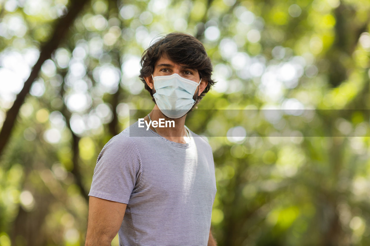 Handsome man wearing a medical protective mask on his face on a sunny day at park.