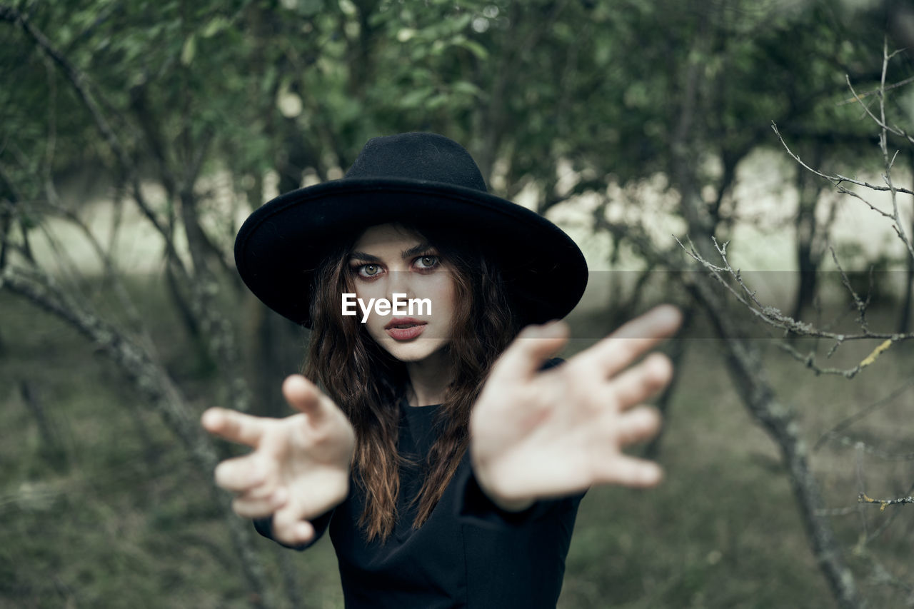 young woman wearing hat standing against trees