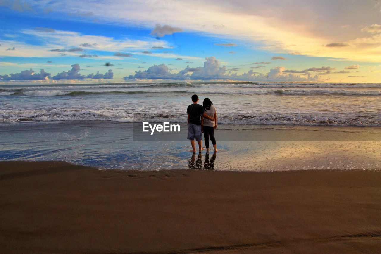 REAR VIEW OF FRIENDS ON BEACH AGAINST SKY