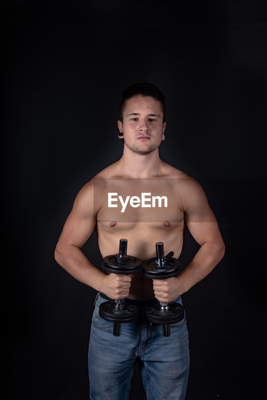 Portrait of shirtless man lifting dumbbells against black background