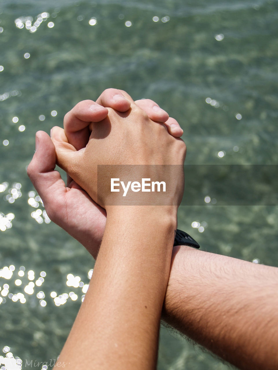 Cropped image of couple holding hands against sea