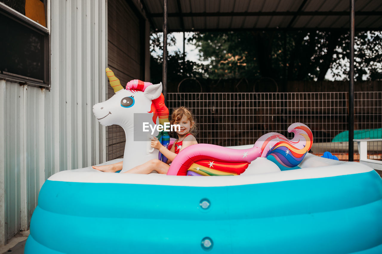 Young girl sitting on inflatible rainbow unicorn in back yard pool