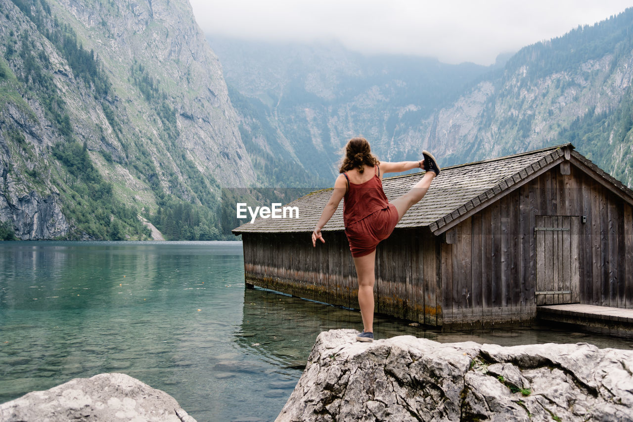 Woman exercising on rock by lake against mountain range