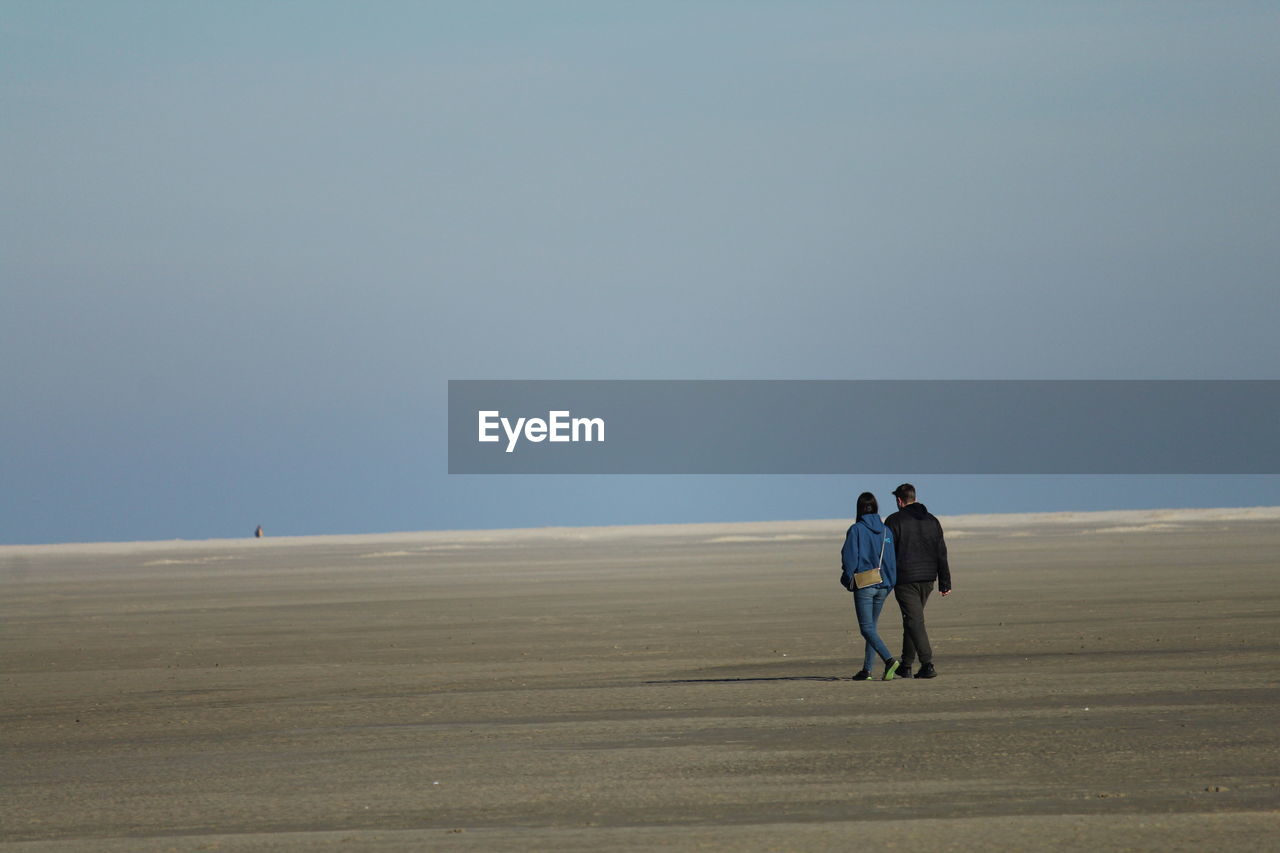 Rear view of man and woman walking on sand