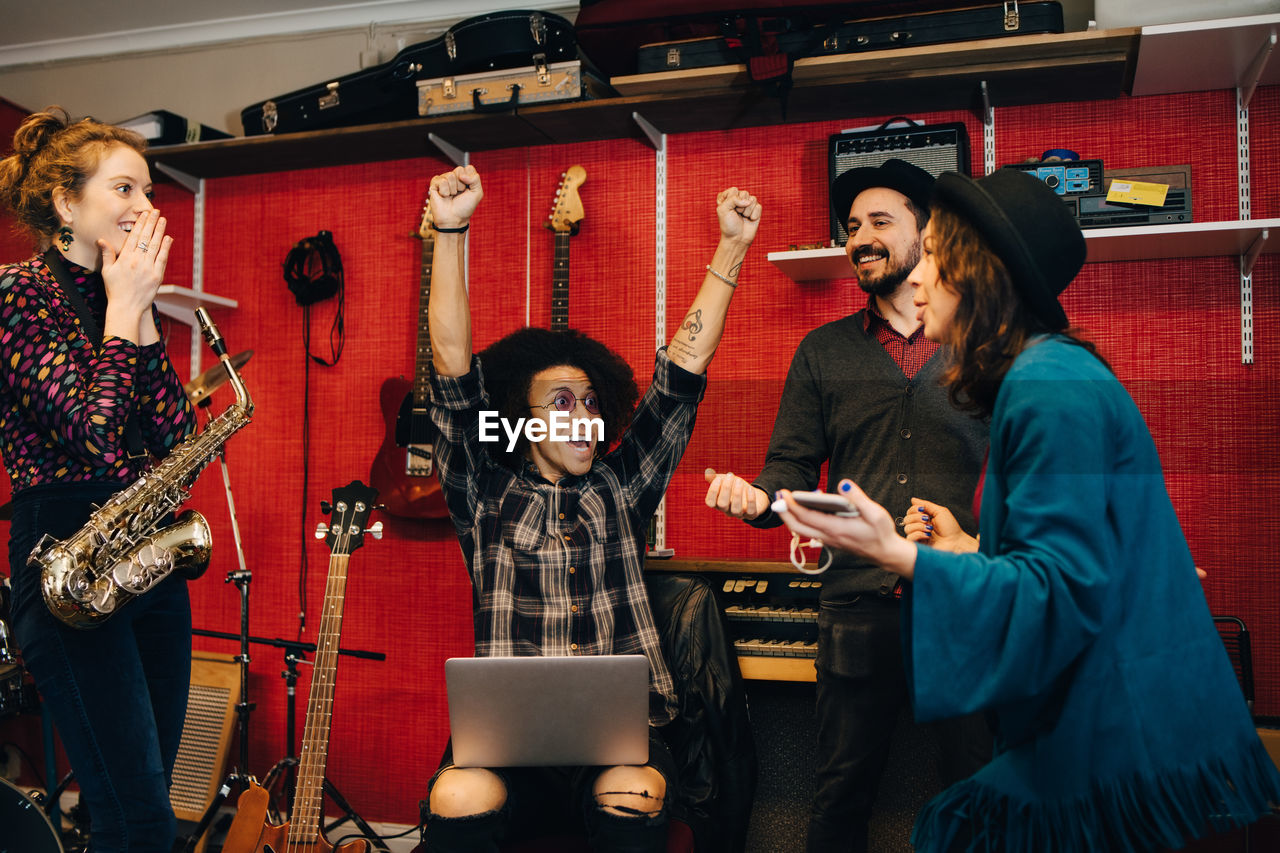 Male and female friends celebrating while standing against instruments at recording studio