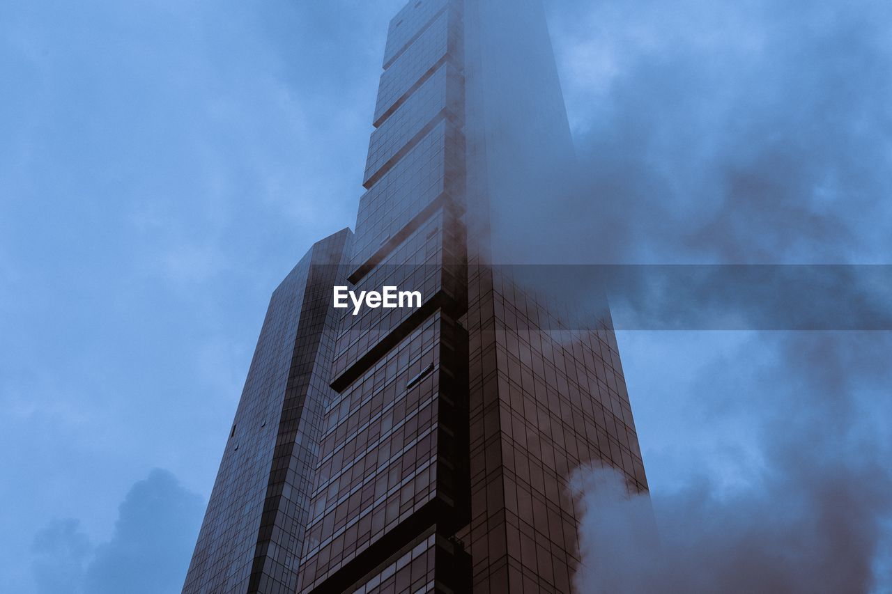 Low angle view of modern building and smoke in city against sky