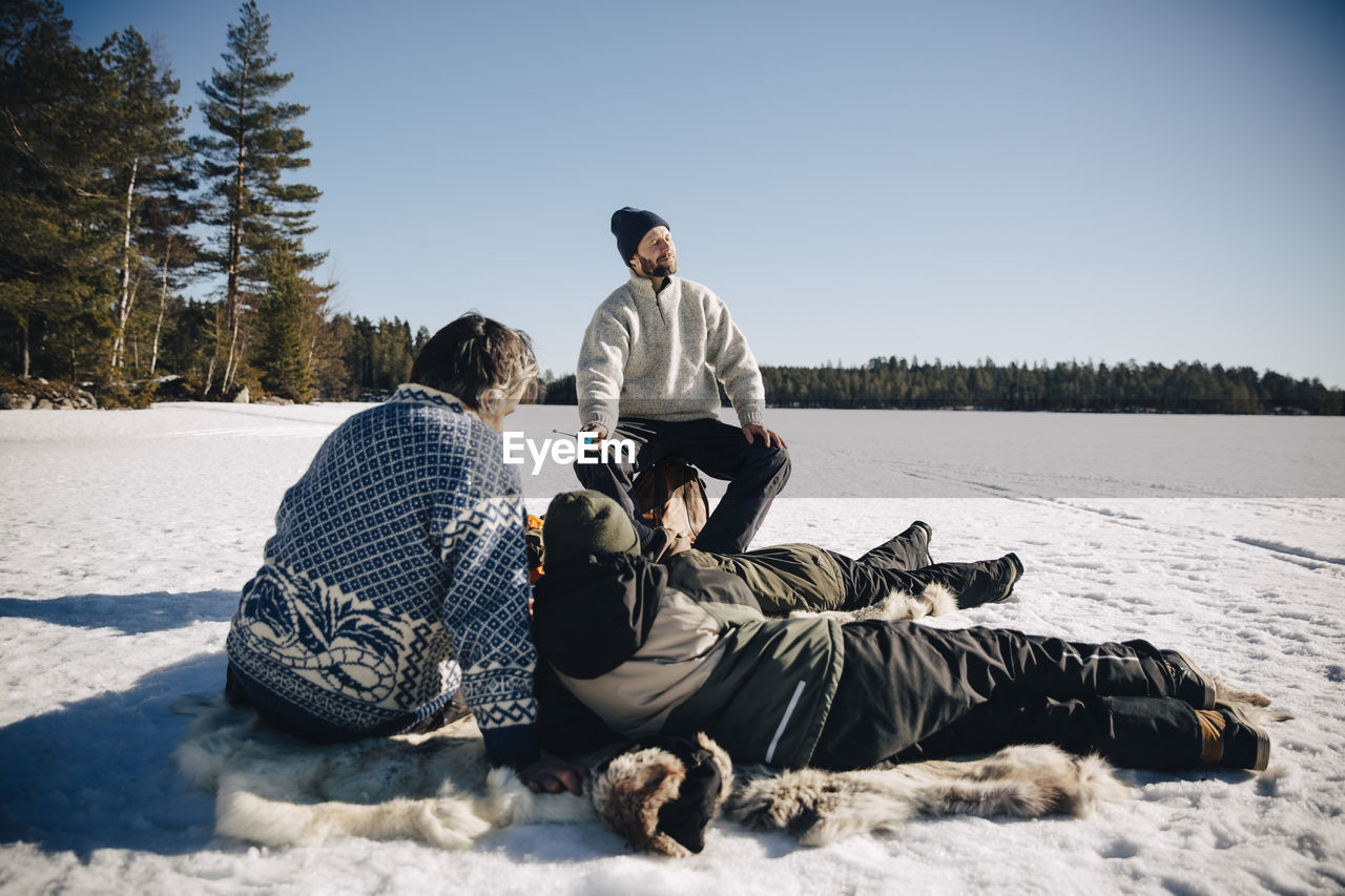 Father and son sitting on animal skin while ice fishing with friends enjoying sunny day in winter