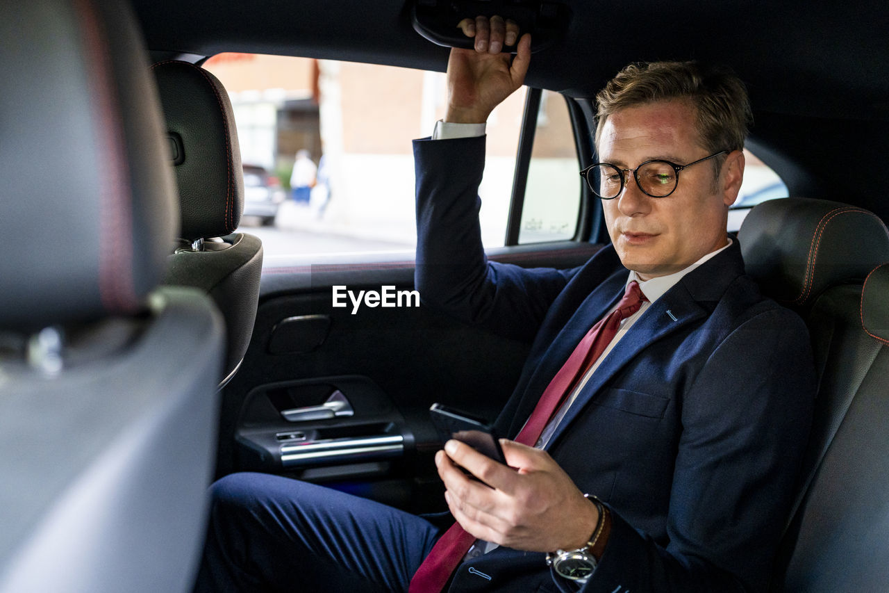 Businessman using smart phone sitting in car